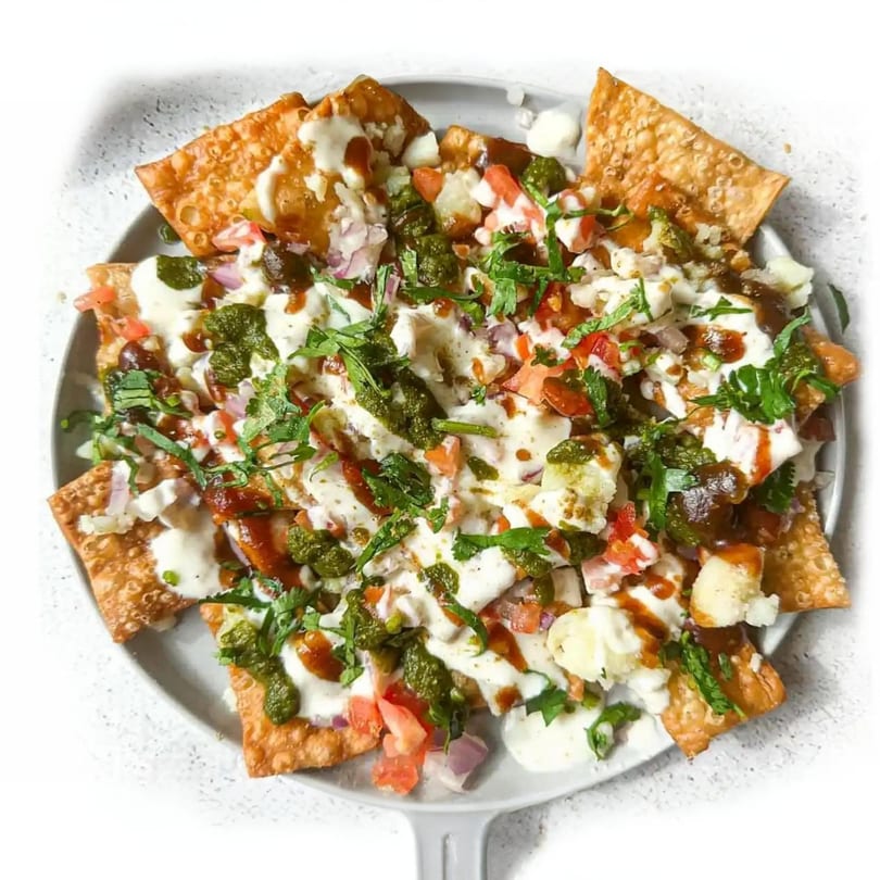 A close-up of Pakistani chaat with crispy flatbread, yogurt, chutneys, and fresh herbs.