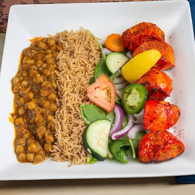 Mehran Restaurant's chicken tikka, chana masala, rice, and fresh salad on a white plate.