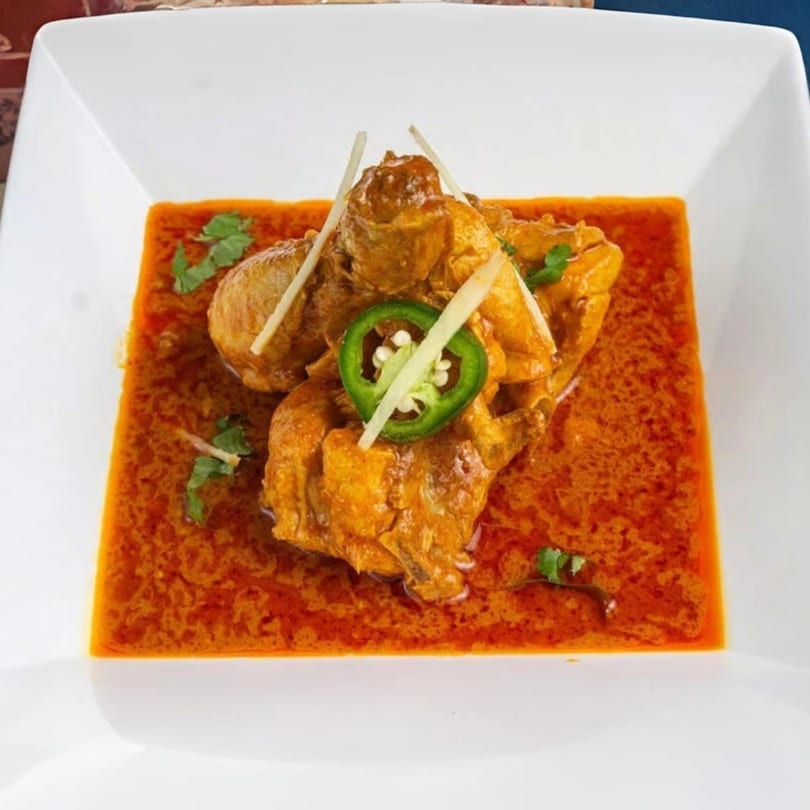 Pakistani chicken karahi with rich red gravy, garnished with ginger slivers, cilantro, and a green chili.