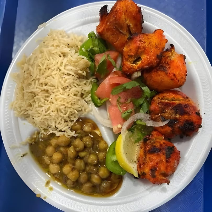 Mehran Restaurant's chicken tikka with rice, chickpea curry, and a side salad on a white plate.